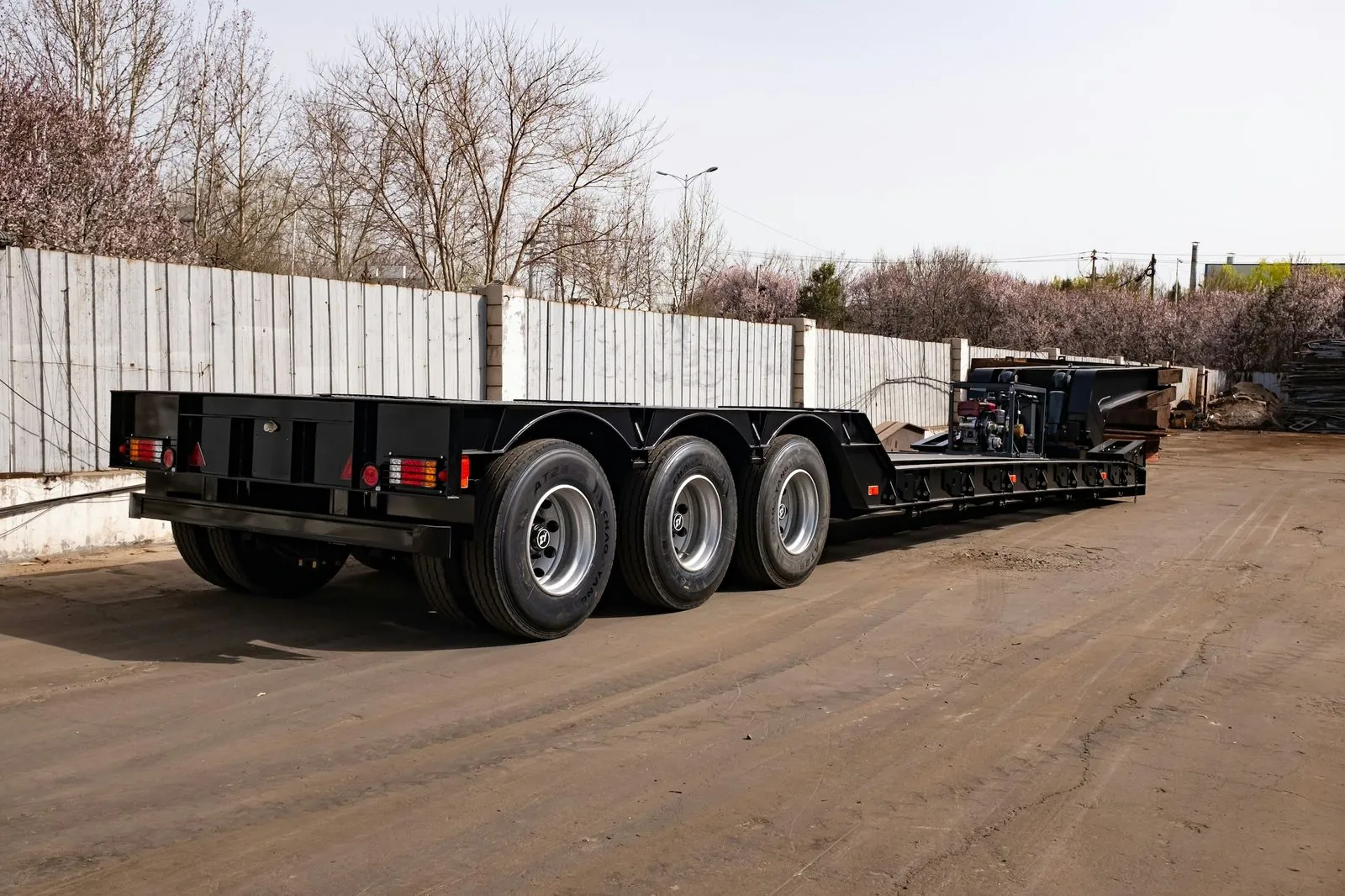 Black triple-axle equipment trailer on a gravel yard
